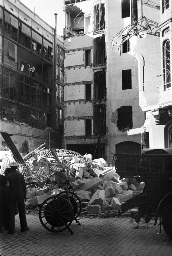 Edifici bombardejat i carro portamànegues i part posterior d’un vehicle de bombers.